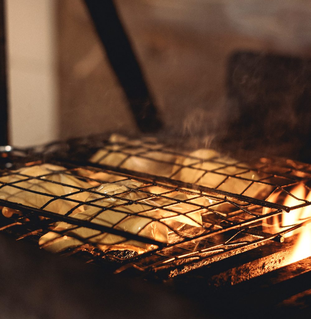 Vista de una parrilla sobre el fuego ardiente con varios paquetes (papillot) de comida horneándose.