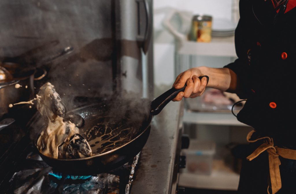 Vista de las manos del cocinero salteando unos mejillones al estilo Tailandés.