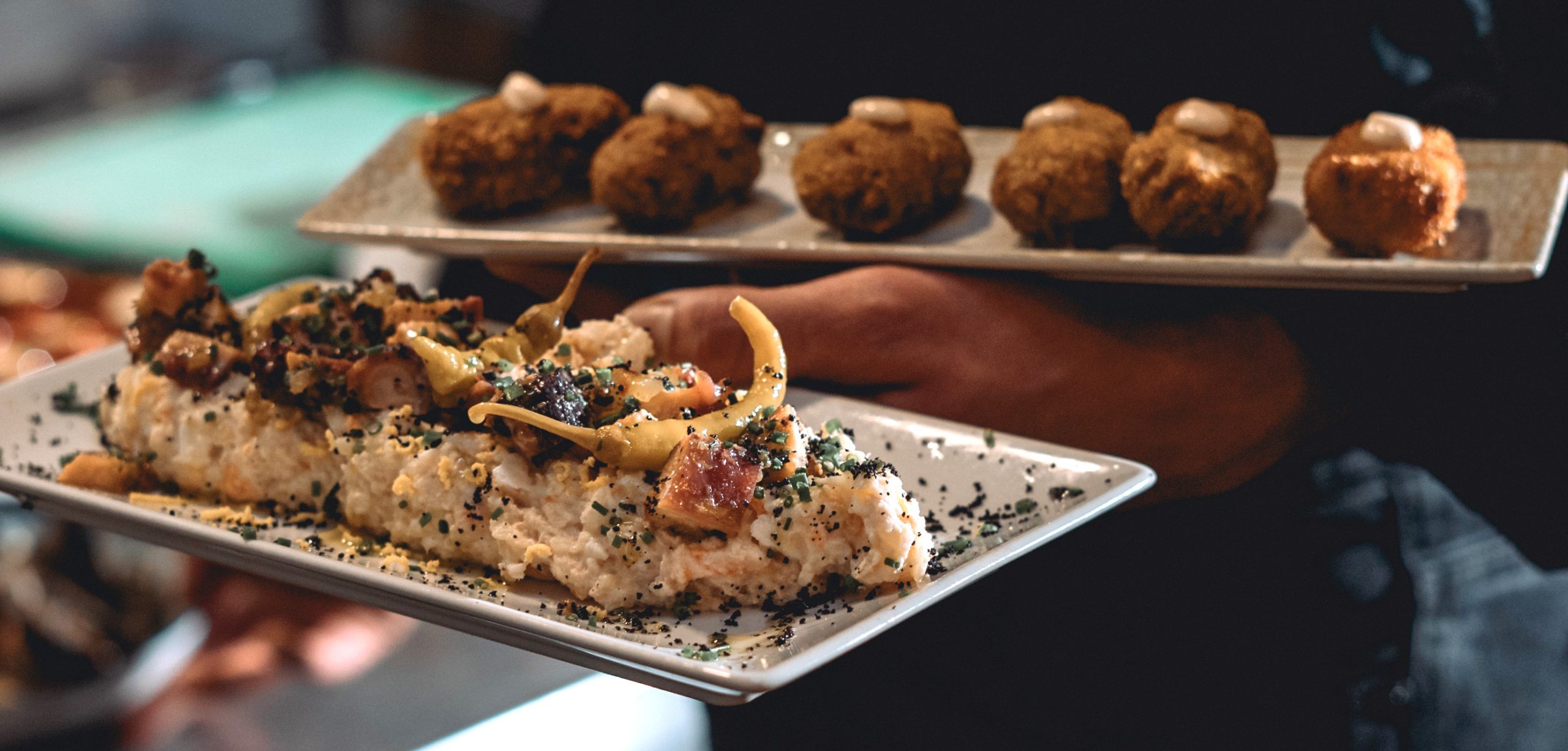 Vista de las manos del camarero con un entrante de ensaladilla y otro de croquetas.