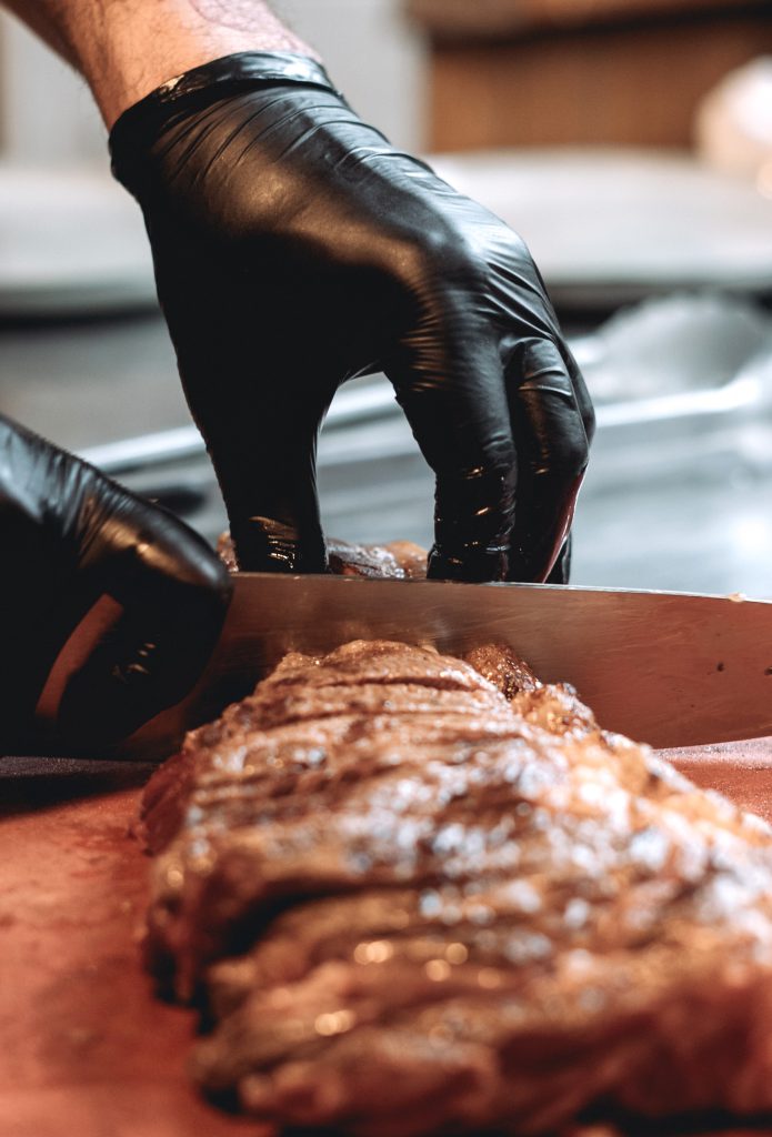 Vista de las manos del cocinero cortando un entrecote braseado en tiras antes de servirlo.